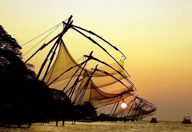  Large Chinese fishing nets silhouetted against a golden sunset over the ocean bottom.