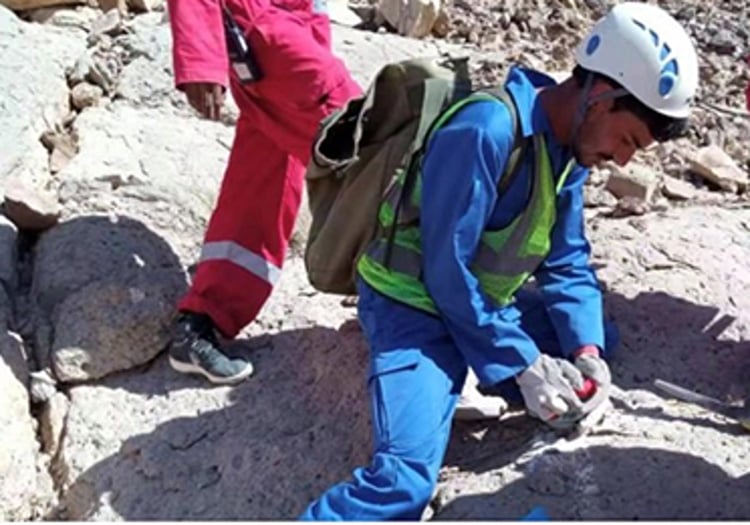 A worker in blue coveralls and a white helmet installs a SmartSolo node for seismic survey on rocky terrain.