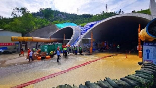 Workers stand outside a tunnel entrance during structural health monitoring, with water flowing out.