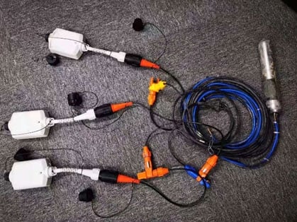 Three white SmartSolo nodes with black and orange connectors are shown with coiled blue and black cables and a silver seismometer.