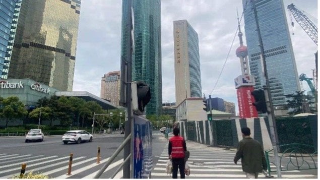 Two people walk across a crosswalk in a city with tall buildings, including the Oriental Pearl Tower.