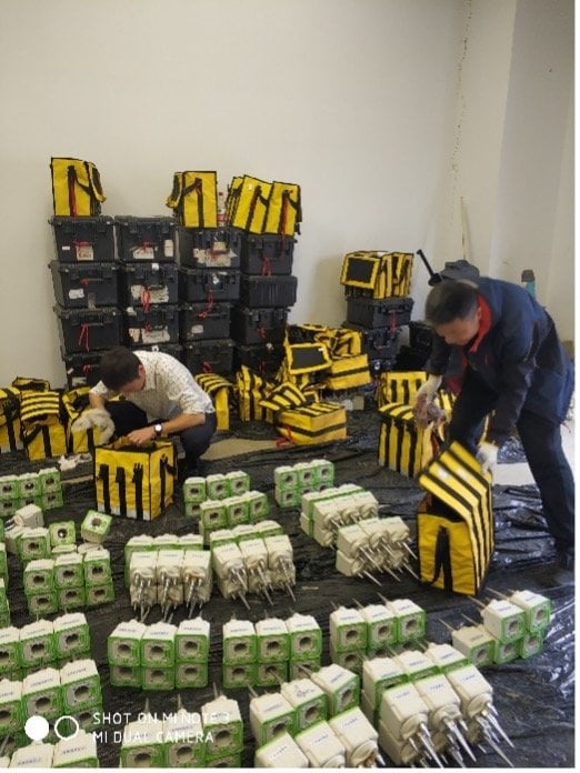 Two workers prepare SmartSolo nodes and seismometers for a seismic survey, surrounded by equipment bags and storage boxes.