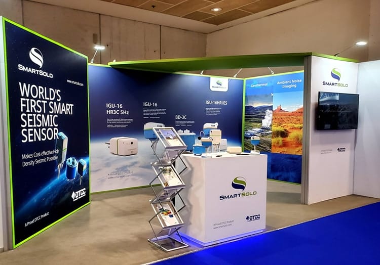SmartSolo booth with "WORLD'S FIRST SMART SEISMIC SENSOR" banner, displaying various seismometer nodes for geophysical exploration.