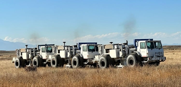 A line of seismic vibrator trucks used for seismic survey and geophysical exploration in a field.