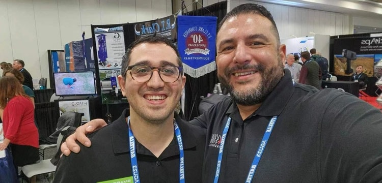 Two men smile at a trade show booth with a banner that reads "R.T. Clark Companies 40th Anniversary Equipment Sales".