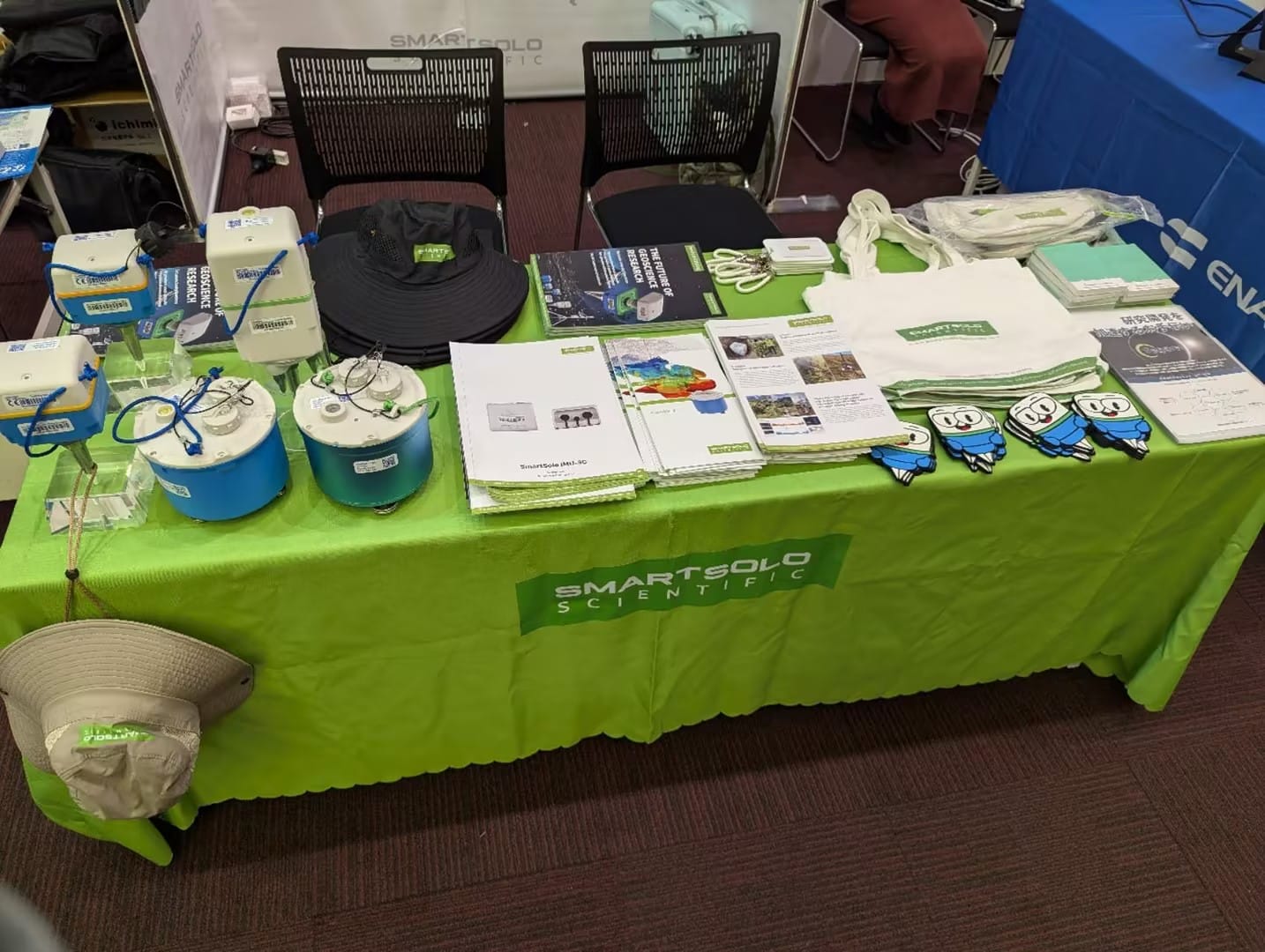SmartSolo Scientific booth table with seismic exploration nodes, seismometers, brochures, hats, and tote bags for geophysical exploration.