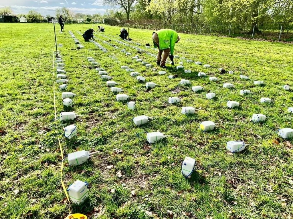 Workers deploy SmartSolo nodes for seismic survey and geophysical exploration in a grassy field.