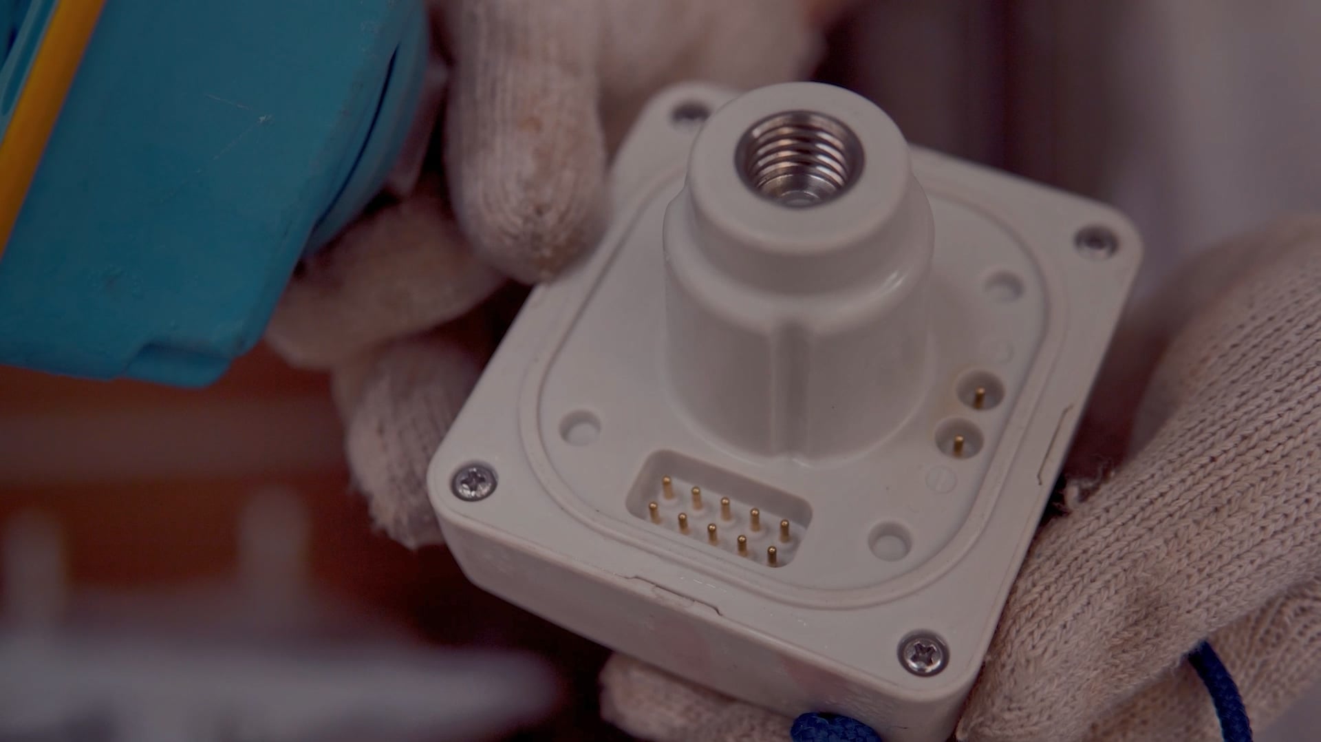 Close-up of a SmartSolo seismometer node base with connection pins and threaded mount, held by a gloved hand.