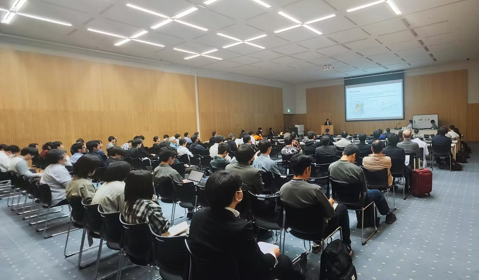 Attendees at a seismology conference presentation, focused on earthquake monitoring and seismic activity, with a screen displaying data.