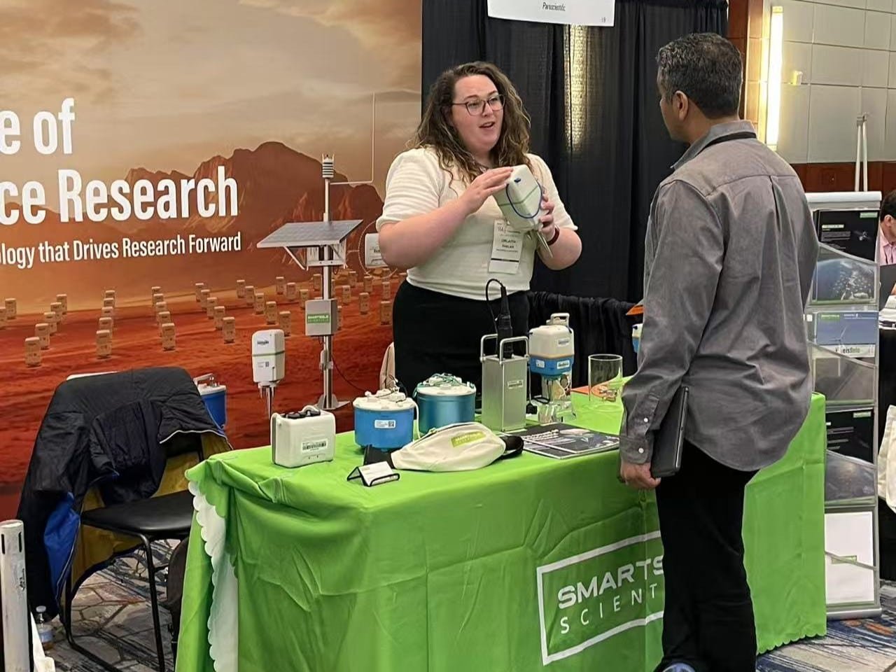 A SmartSolo Scientific representative at booth demonstrates a seismic node for earthquake monitoring and geophysical exploration to a visitor.