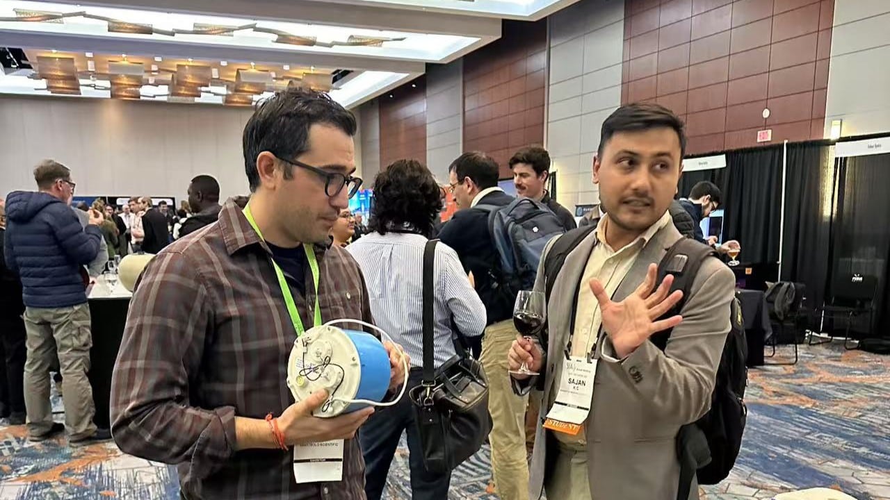 SmartSolo representative and a visitor discuss a SmartSolo Scientific seismometer node for seismic activity monitoring and geophysical exploration at a conference.